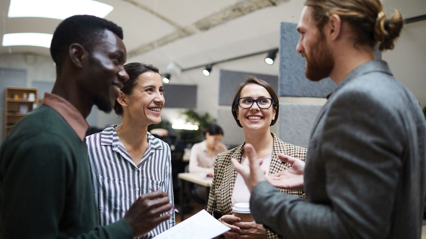 Waist up portrait of diverse group of business people laughing happily while chatting during coffee break in office.