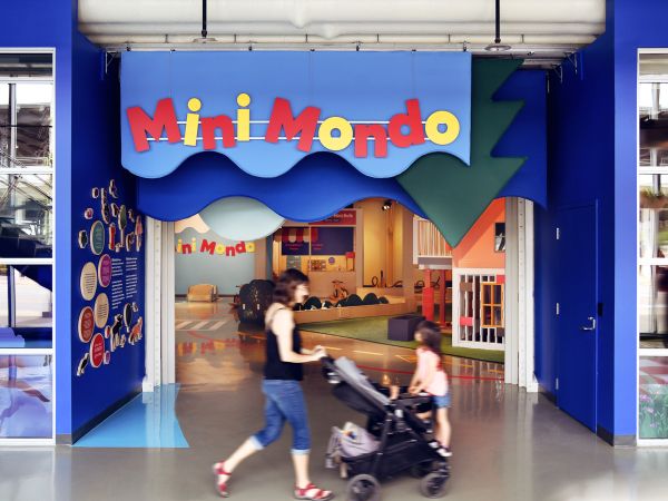 A woman pushes a child in a stroller past the entrance to the Mini Mondo exhibition